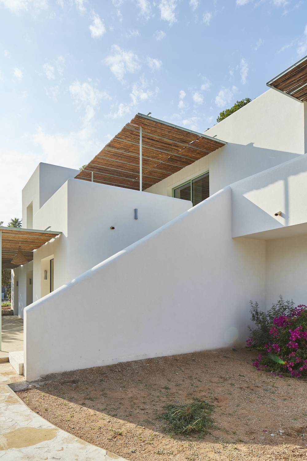 Fachada blanca con cubierta de cañizo y escalera exterior, reforma Na Xamena, Ibiza