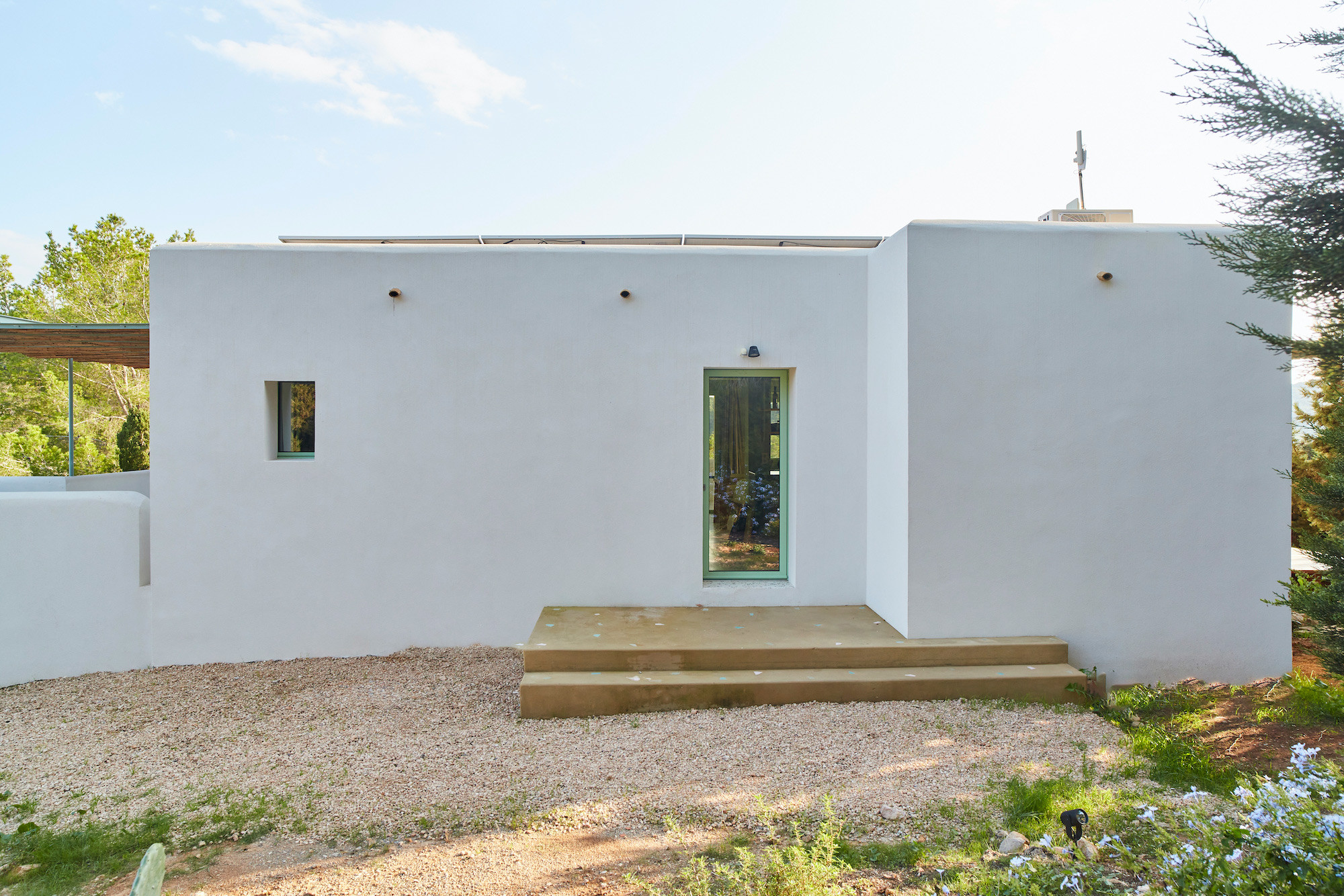 Fachada blanca minimalista con carpintería verde, reforma Na Xamena, Ibiza
