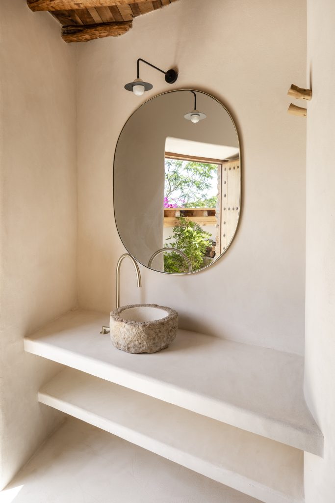 Proyecto de interiorismo de la vivienda Can Duarte de KLARQ con un espejo que refleja la vegetación exterior en un baño minimalista.