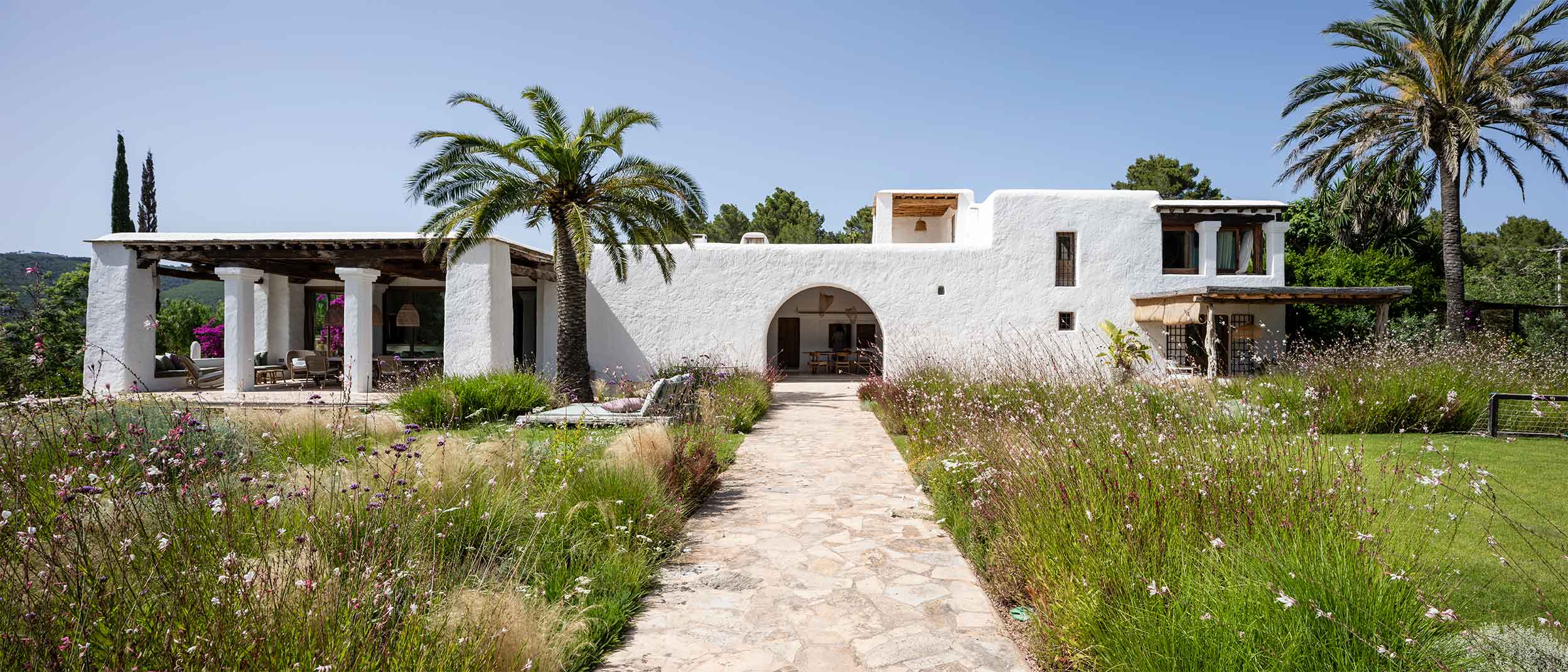 Vivienda reformada por el estudio de arquitectura KLARQ en Ibiza con muros blancos hacia un interior con mobiliario rústico.